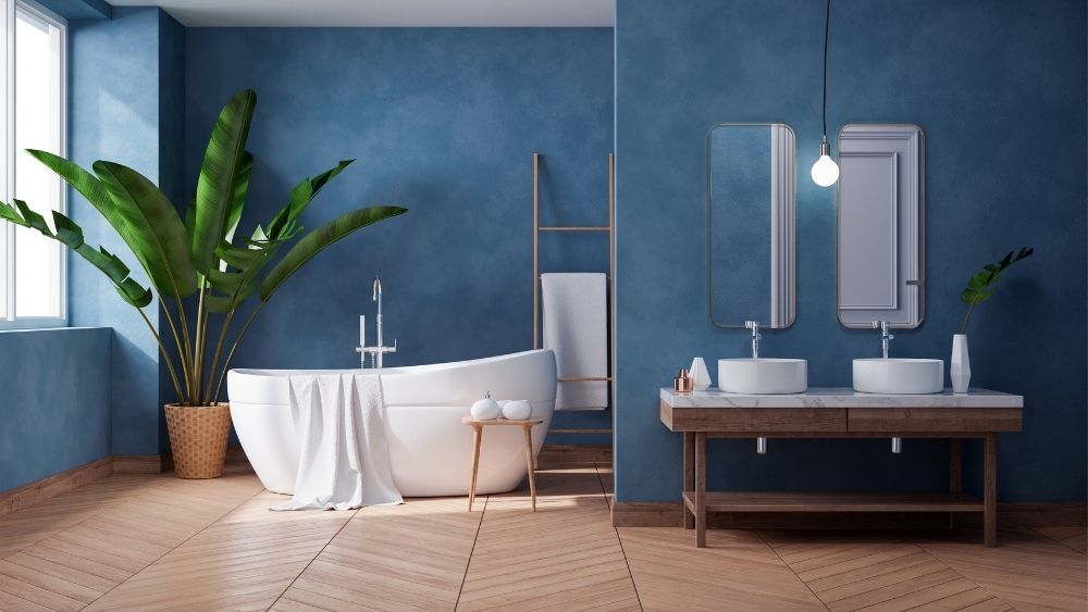 Μοντέρνο όμορφο μπάνιο με λευκή μπανιέρα μπλε τοίχο, διακοσμητική γλάστρα και διπλό μαρμάρινο νιπτήρα.