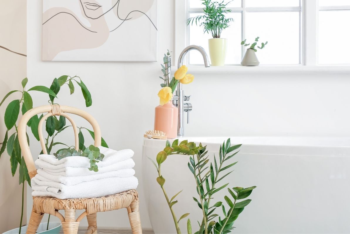Φυτά στο μπάνιο με λευκά είδη υγιεινής, πλακάκια και καρέκλα από μπαμπού.