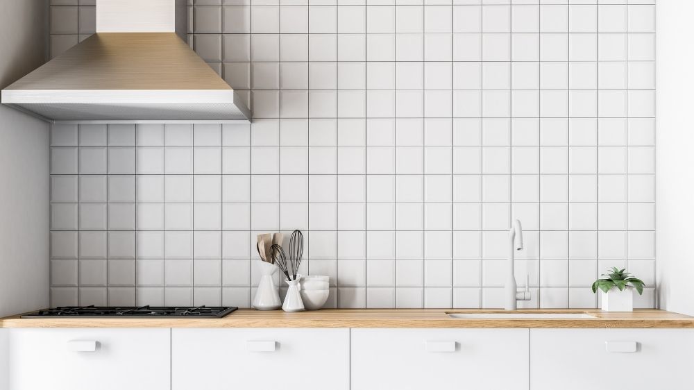 Πάγκος κουζίνας με λευκά πλακάκια τοίχου πίσω και άσπρα συρτάρια.