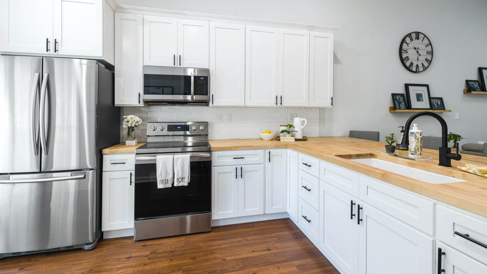 Ξύλινος πάγκος σε λευκή κουζίνα συνδυάζεται με μαύρη βρύση και inox συσκευές.