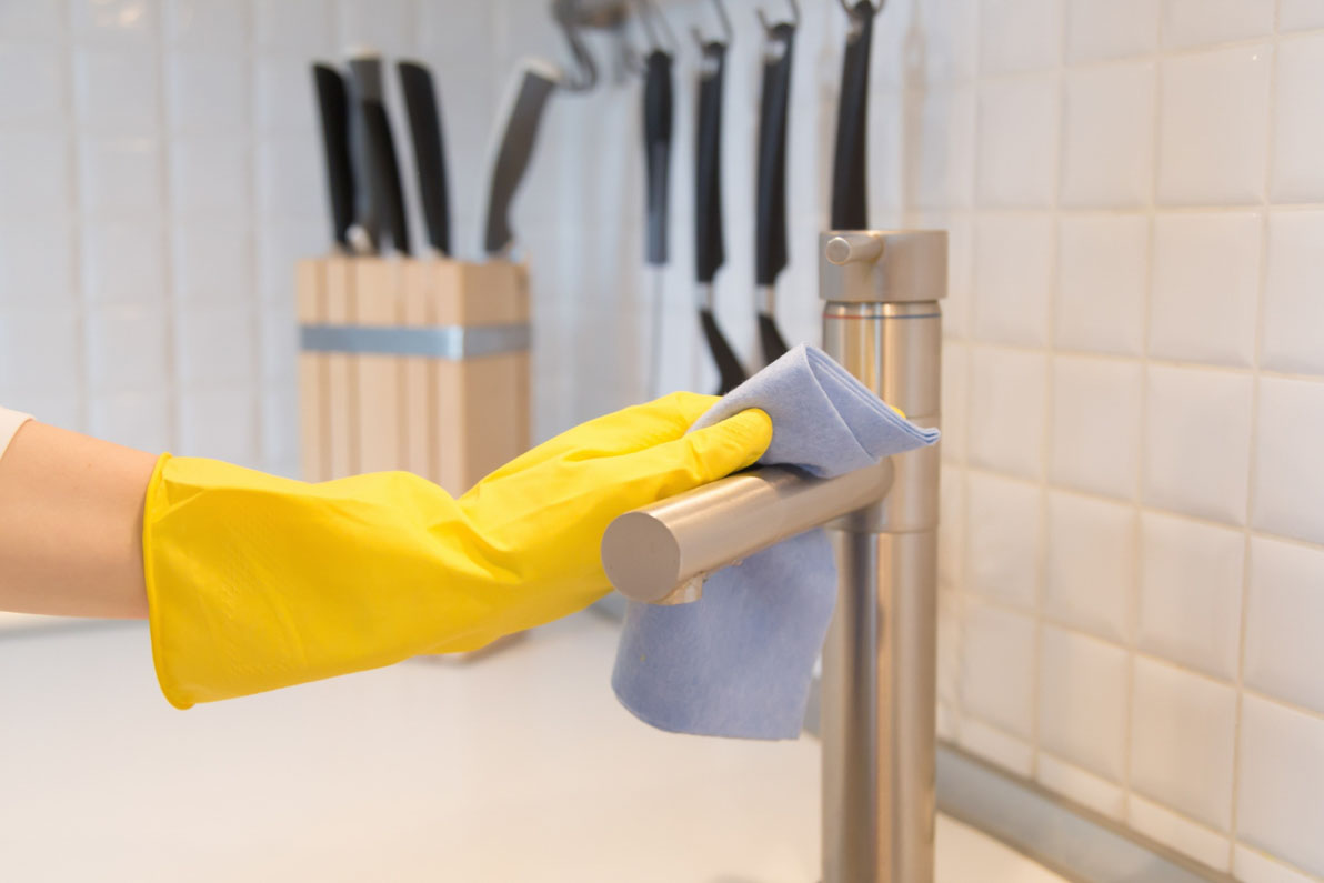 Γυναικείο χέρι με κίτρινο γάντι δείχνει πώς φεύγουν τα άλατα από τις βρύσες, καθαρίζοντας μια μπαταρία κουζίνας με πανί.