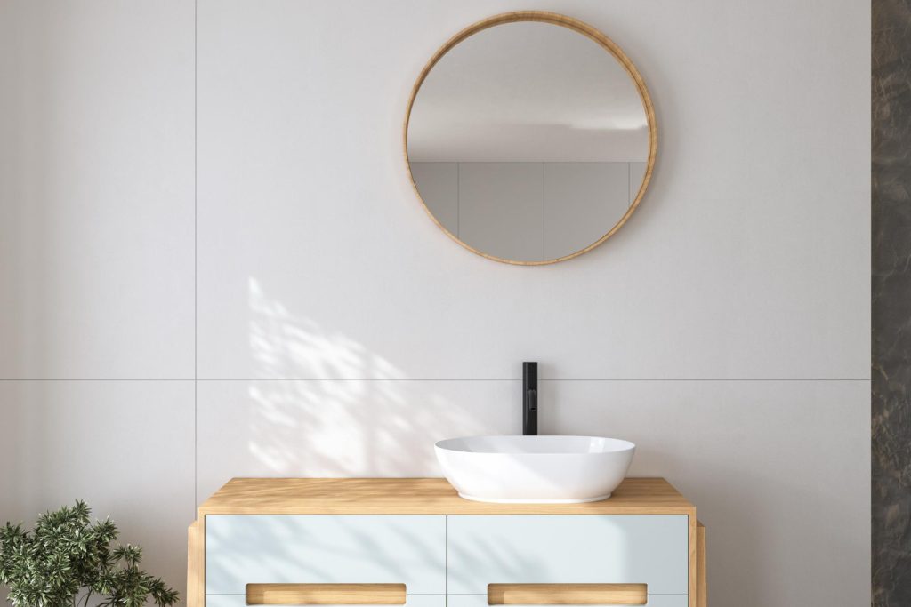 Στρογγυλός καθρέφτης μπάνιου με ξύλινο πλαίσιο περιμετρικά, πάνω από νιπτήρα.