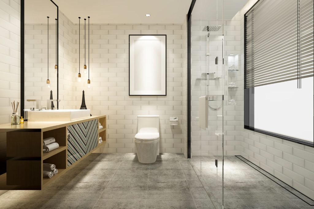 Μοντέρνα χτιστή ντουζιέρα με γυάλινο διαχωριστικό και γκρι πλακάκια δαπέδου, ενιαία με το υπόλοιπο μπάνιο.
