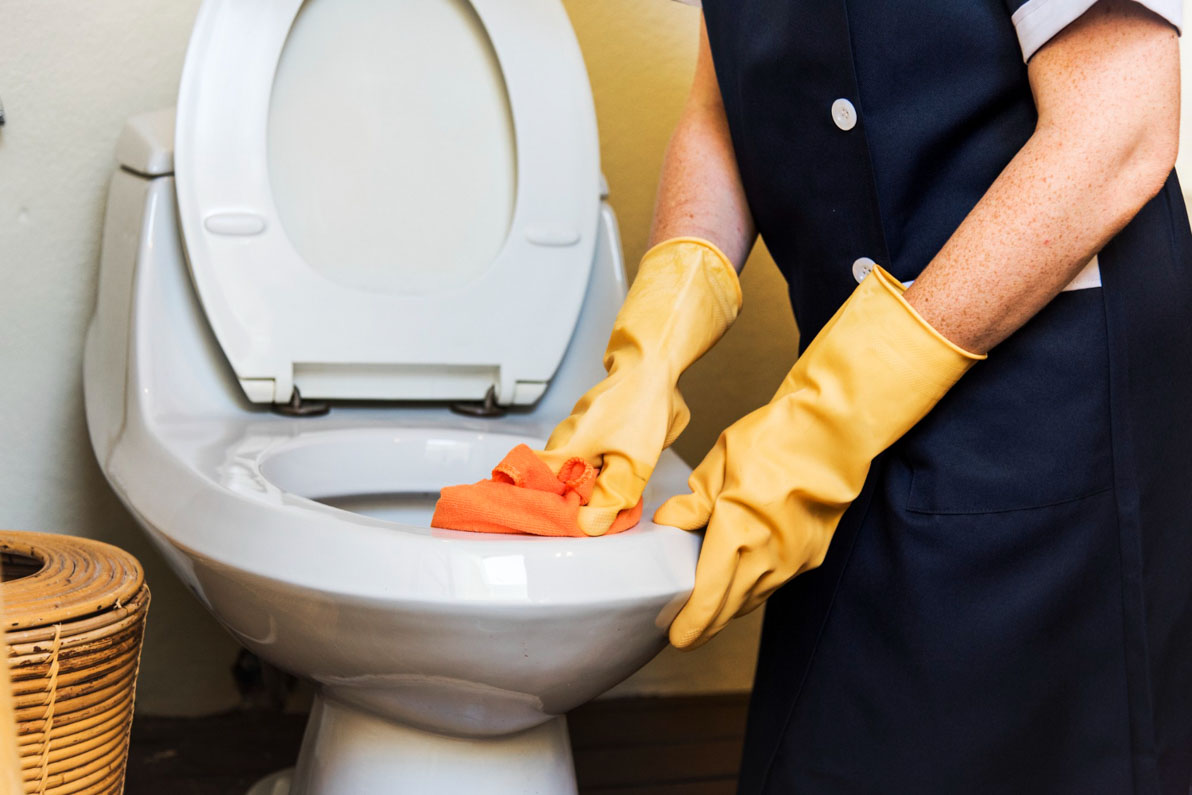 Θεματική για το πώς καθαρίζουμε τη λεκάνη της τουαλέτας. Γυναίκα με κίτρινα γάντια τρίβει με πανί τη λεκάνη.