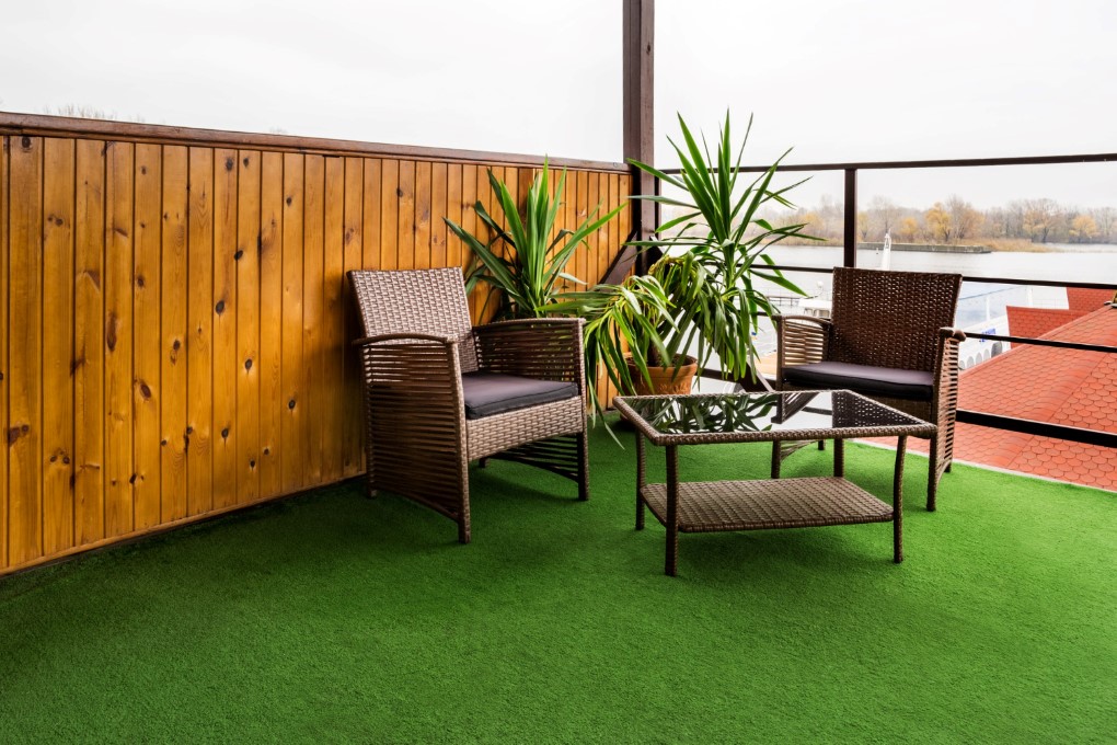Μπαλκόνι στο πάτωμα του οποίου υπάρχει πράσινος τάπητας. Καφέ καρέκλες και τραπεζάκι βρίσκονται στη γωνία της βεράντας.
