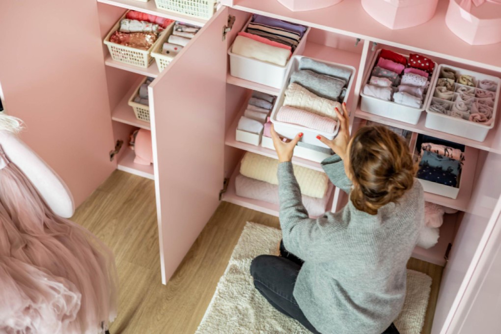 Θεματική εικόνα για συμβουλές για οργάνωση σπιτιού. Γυναίκα τακτοποιεί ρούχα σε κουτιά αποθήκευσης μέσα σε ροζ συρταριέρα.